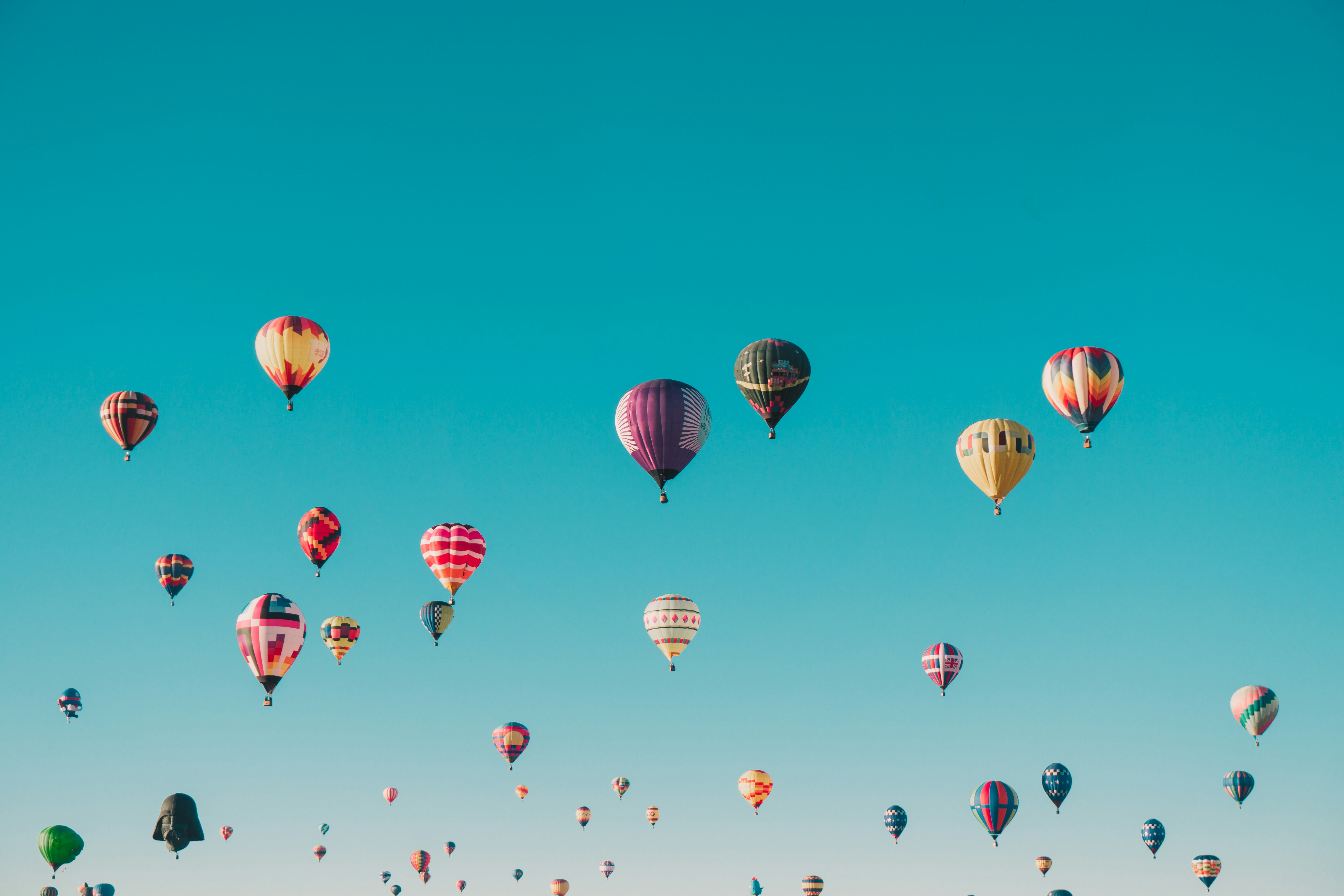 Numerous colorful hot air balloons floating in a clear blue sky.