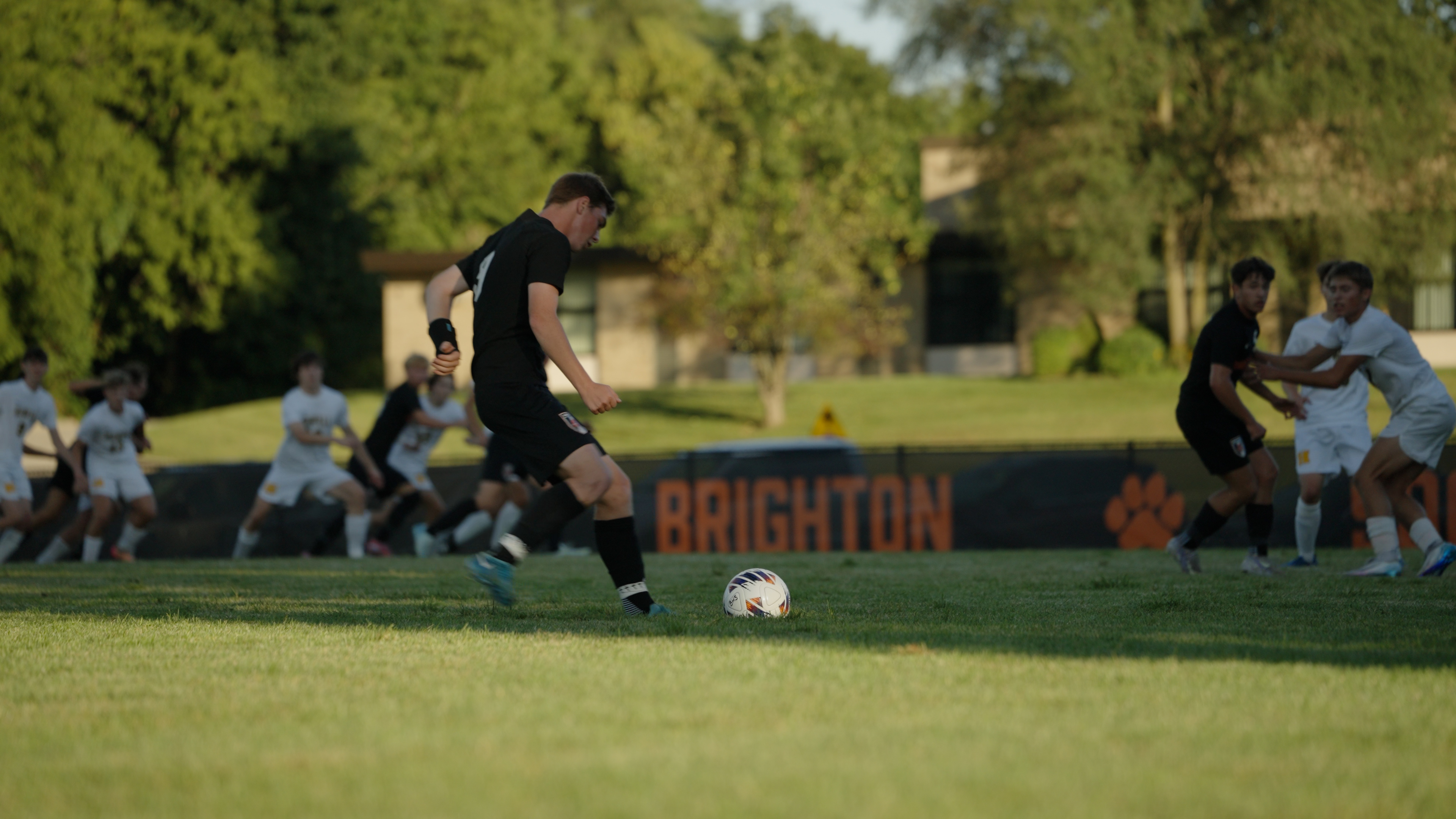 Soccer player in black uniform preparing to kick a soccer ball on a grass field during a match.