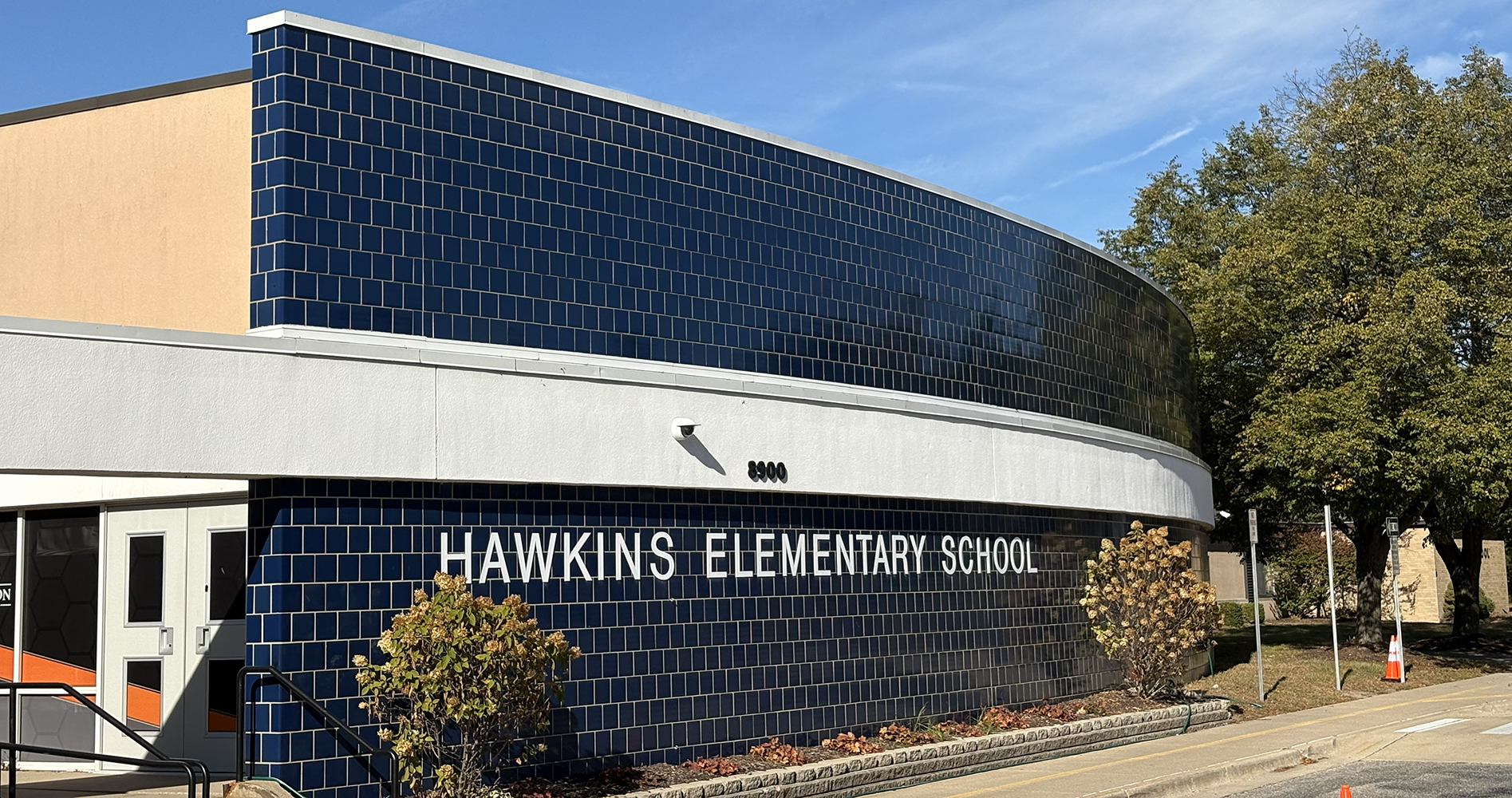 Curved building facade with dark blue tiles and white letters spelling Hawkins Elementary School under a clear blue sky.
