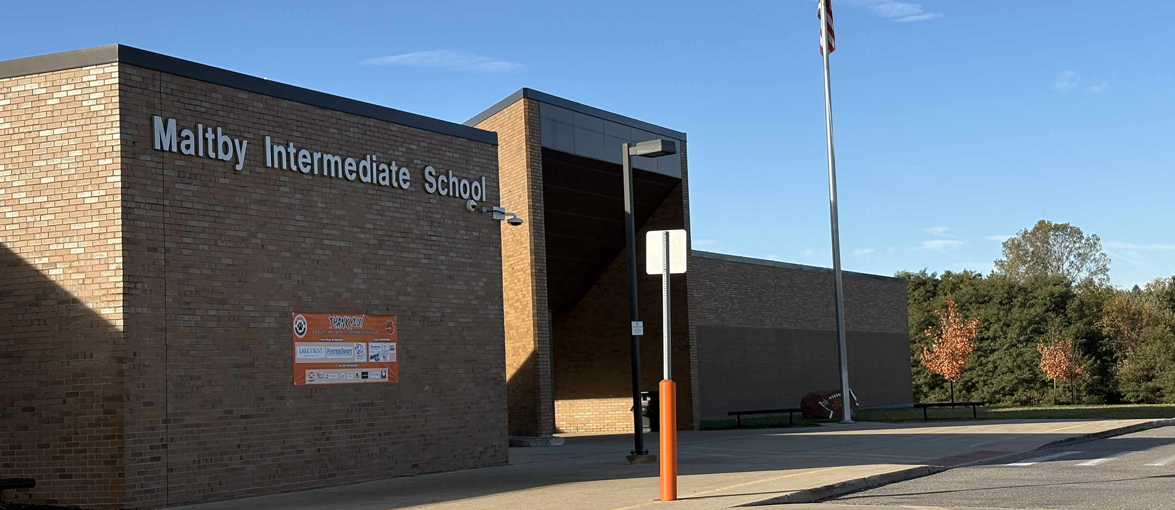 Brick building of Maltby Intermediate School with a flagpole and autumn trees in the background under a clear blue sky.