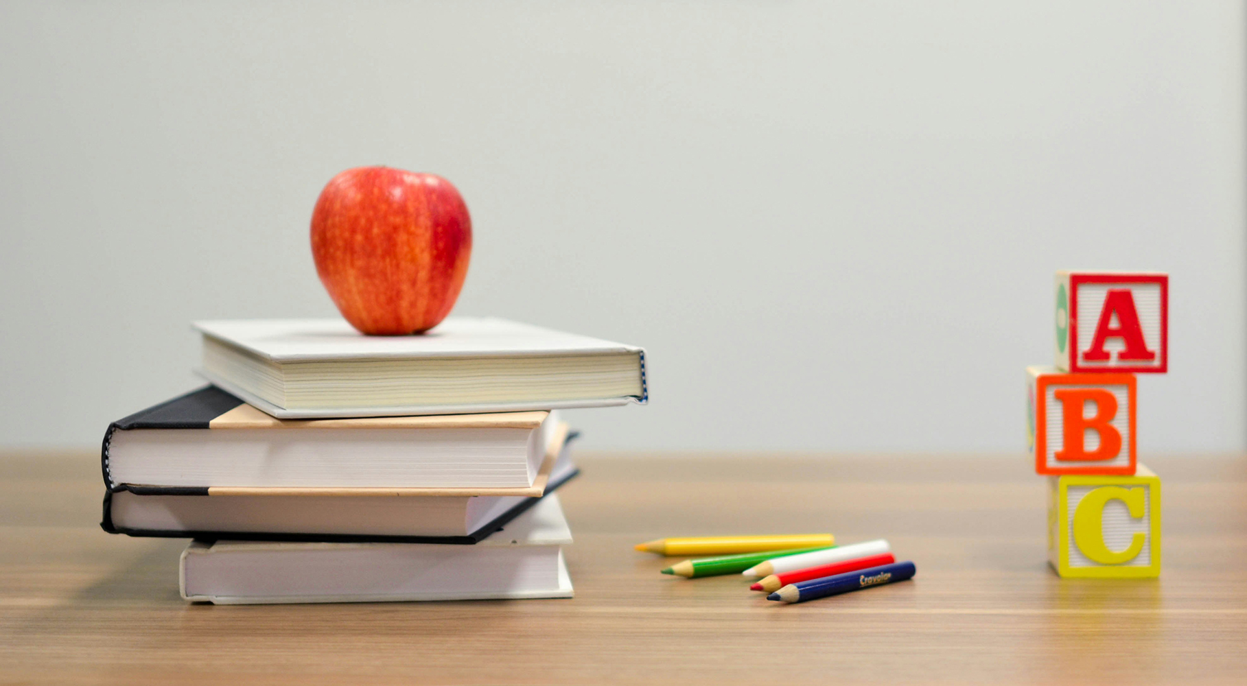 Red apple on top of a stack of books with colored pencils and ABC blocks on a wooden table.