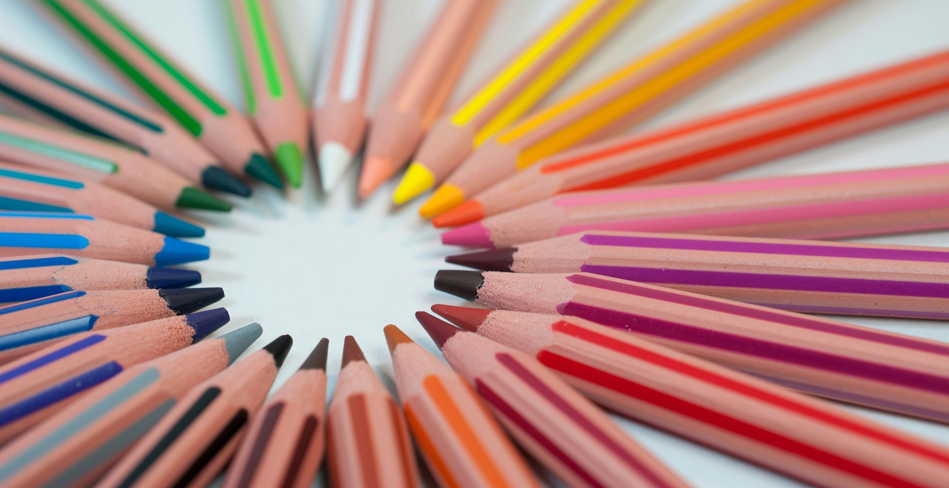 Close-up of colored pencils arranged in a circular pattern with sharpened tips pointing inward.