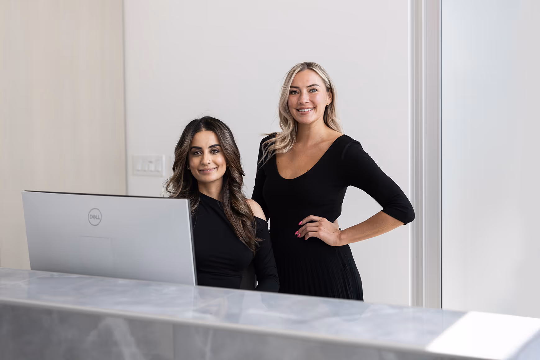 Two women standing in front of a laptop computer.