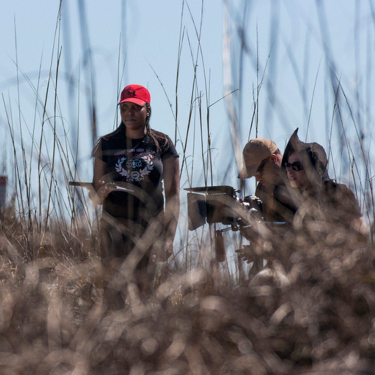 Field shot of three people filming behind brush