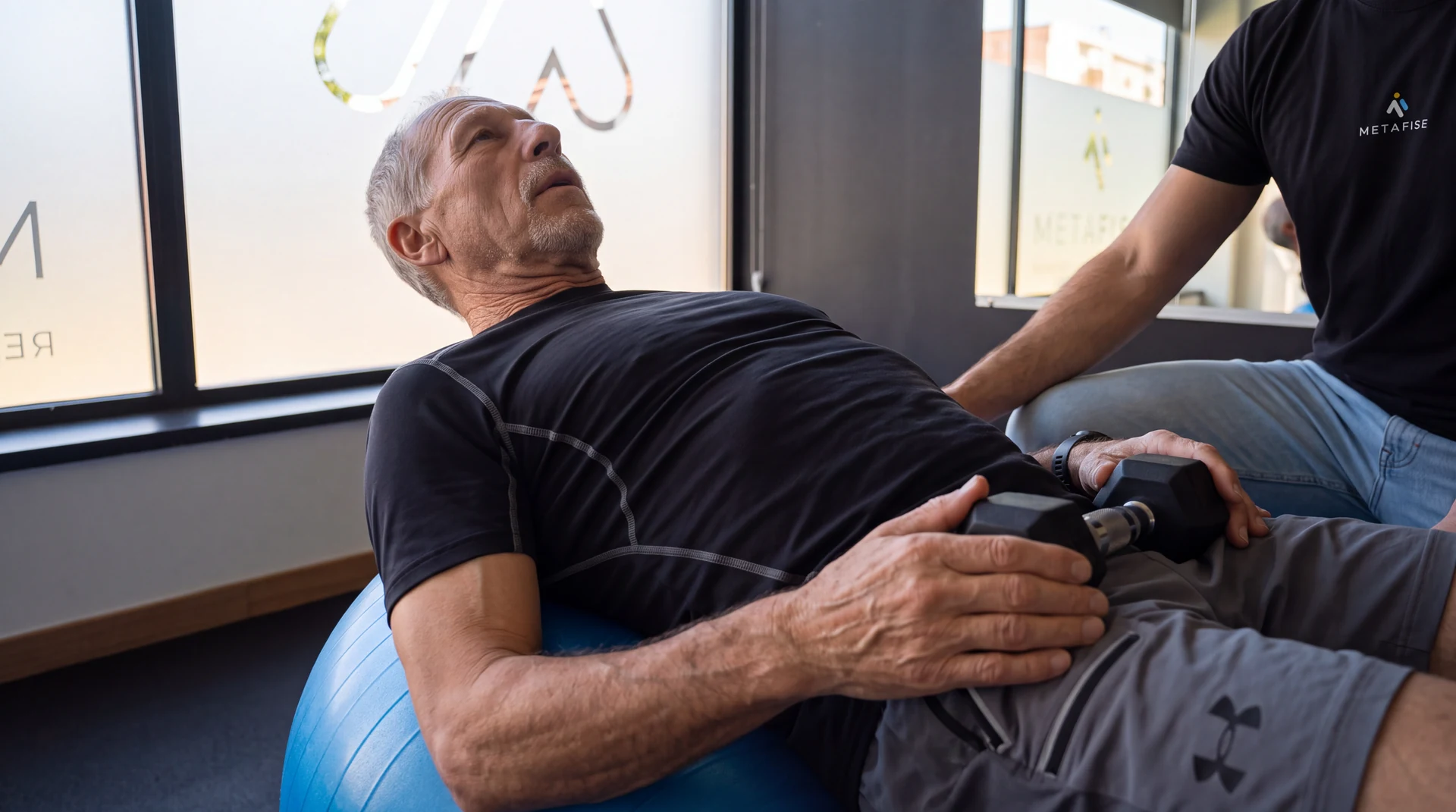 Utente realiza exercício apoiado numa bola, acompanhado pelo fisioterapeuta.