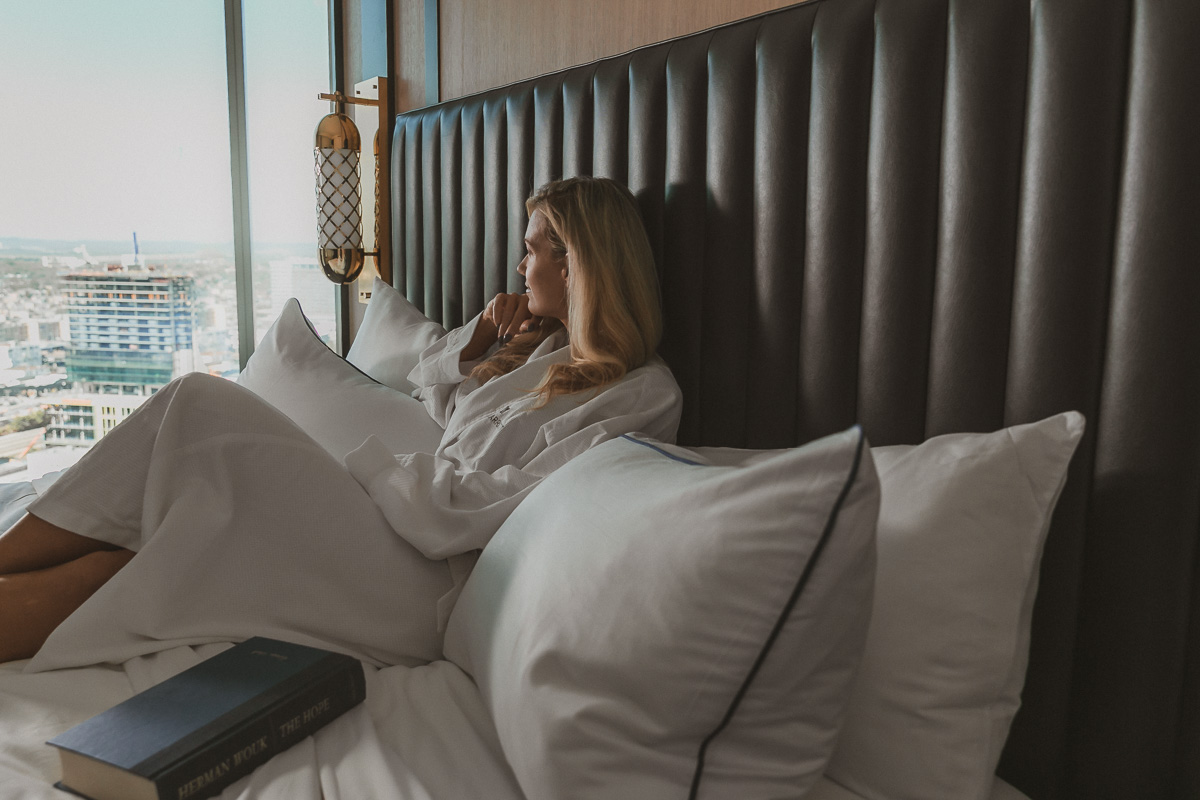 commercial photo of a woman sitting on a hotel bed looking out the window