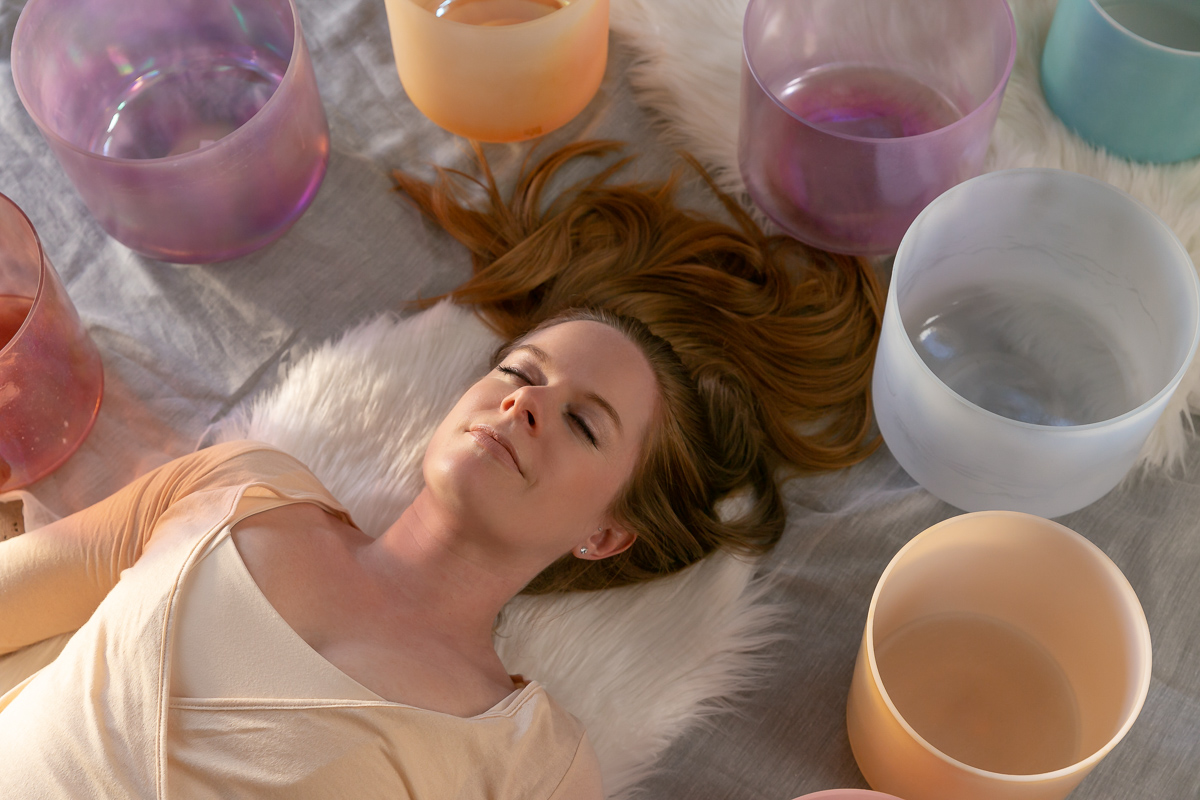 commercial photography of a woman laying down with her eyes closed surrounded by sound bowls