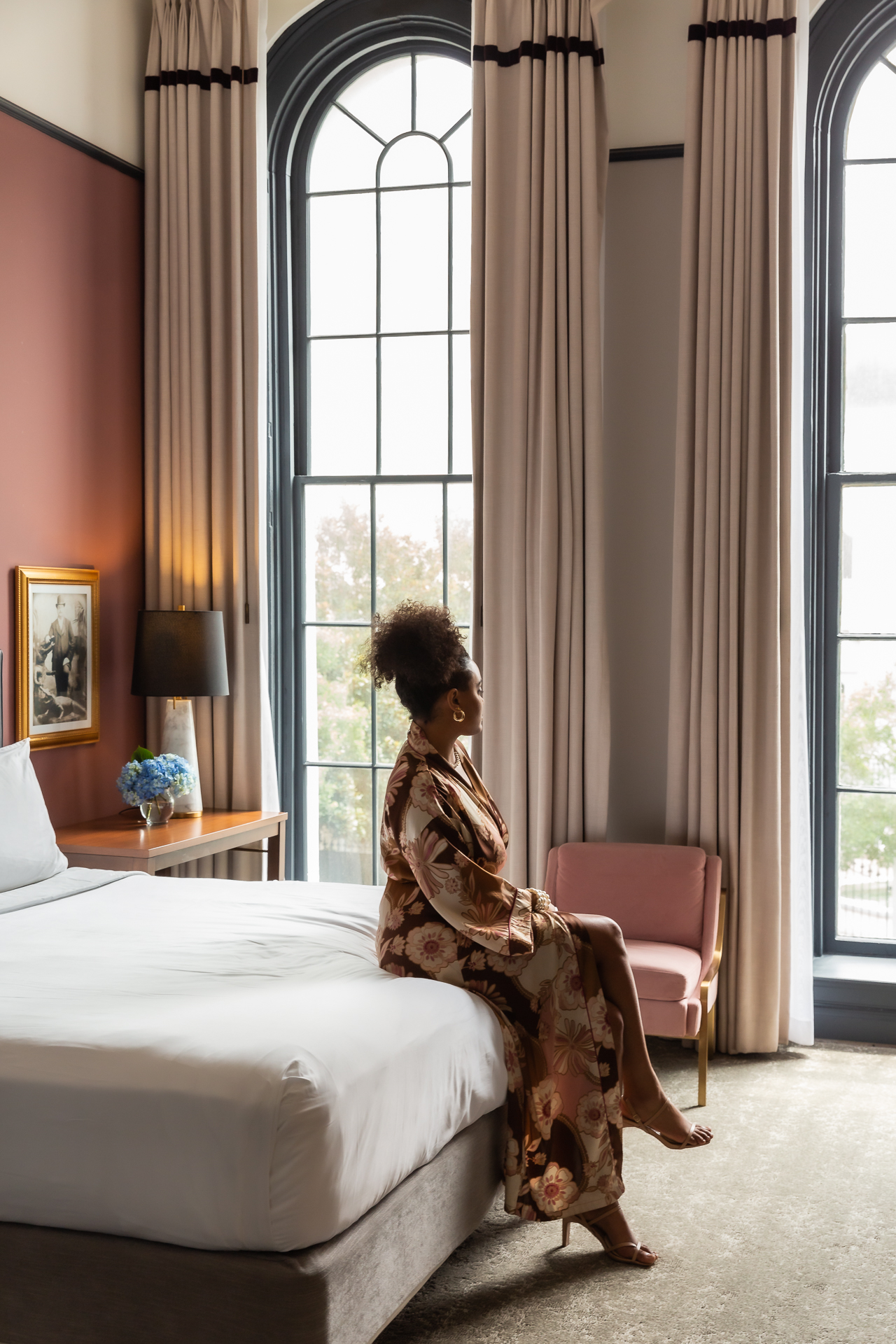 a woman sitting on a bed in a hotel room looking out the window