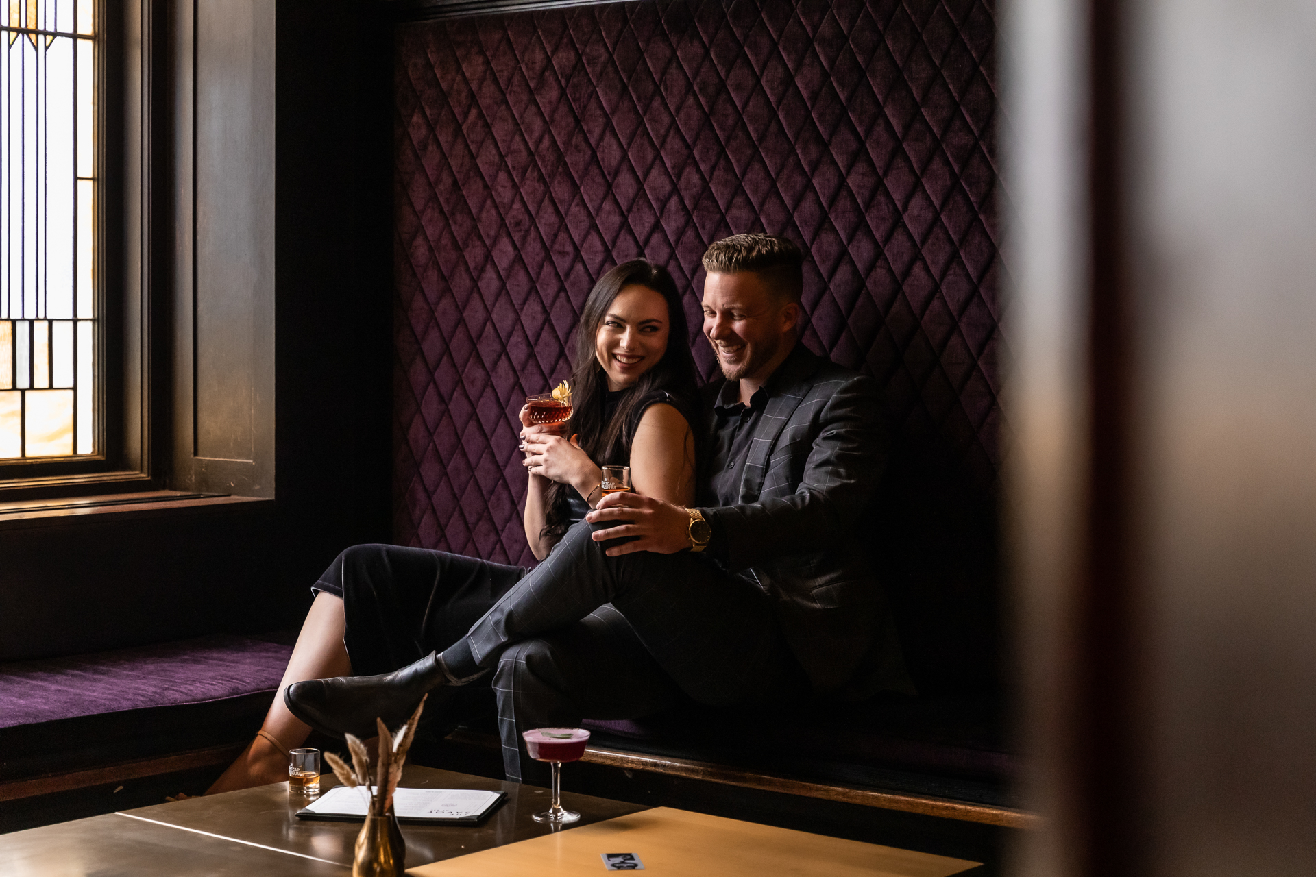 commercial photography of a couple sitting in a bar on a bench seat laughing