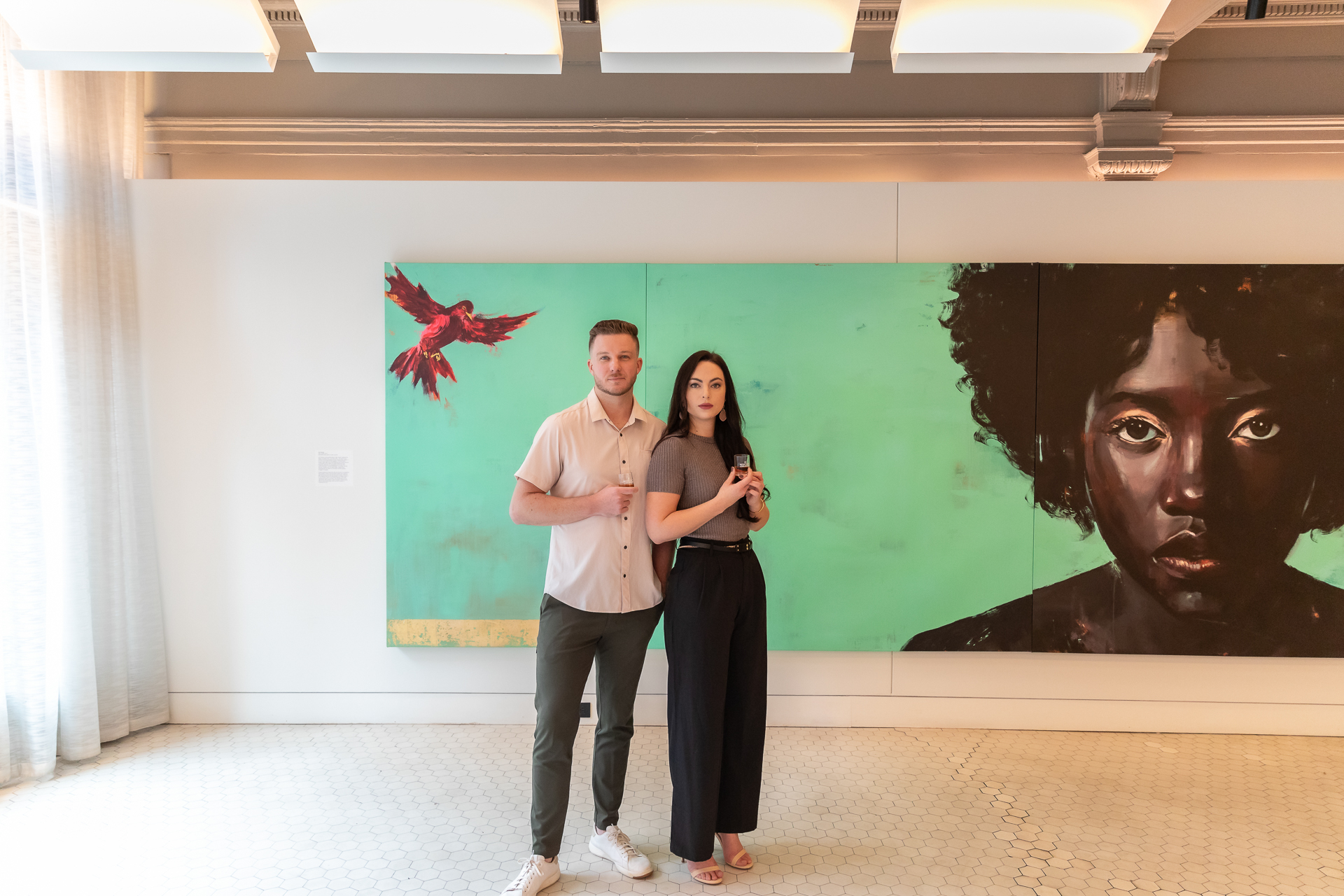 commercial photography at 21C museum hotel of a man and woman standing in front of a large painting featuring a woman and red bird on a green background