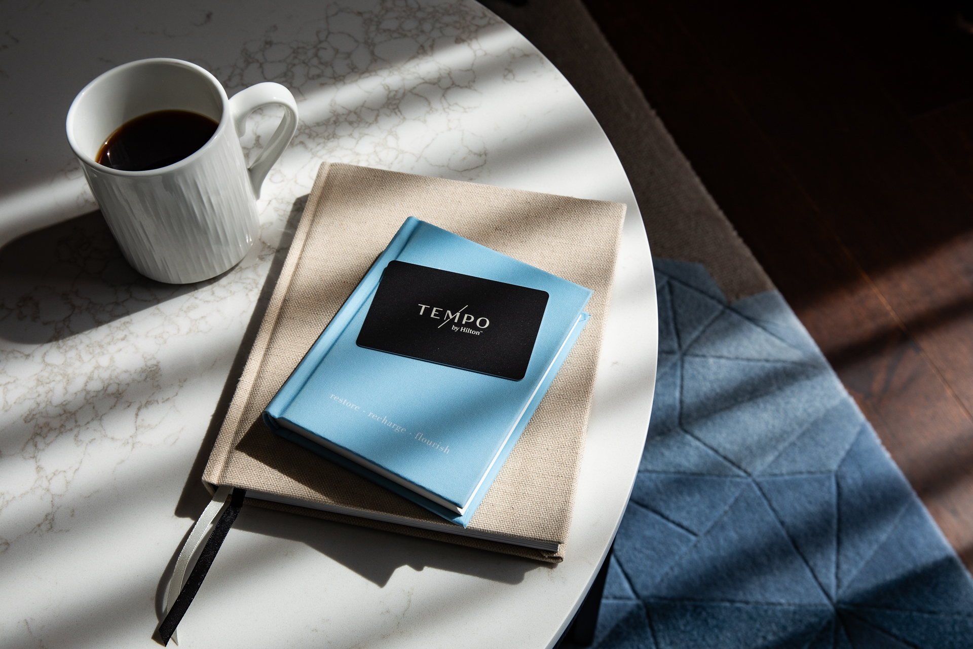 commercial photography of sunlight streaking across a table with notebooks, coffee and a room key for Tempo Nashville