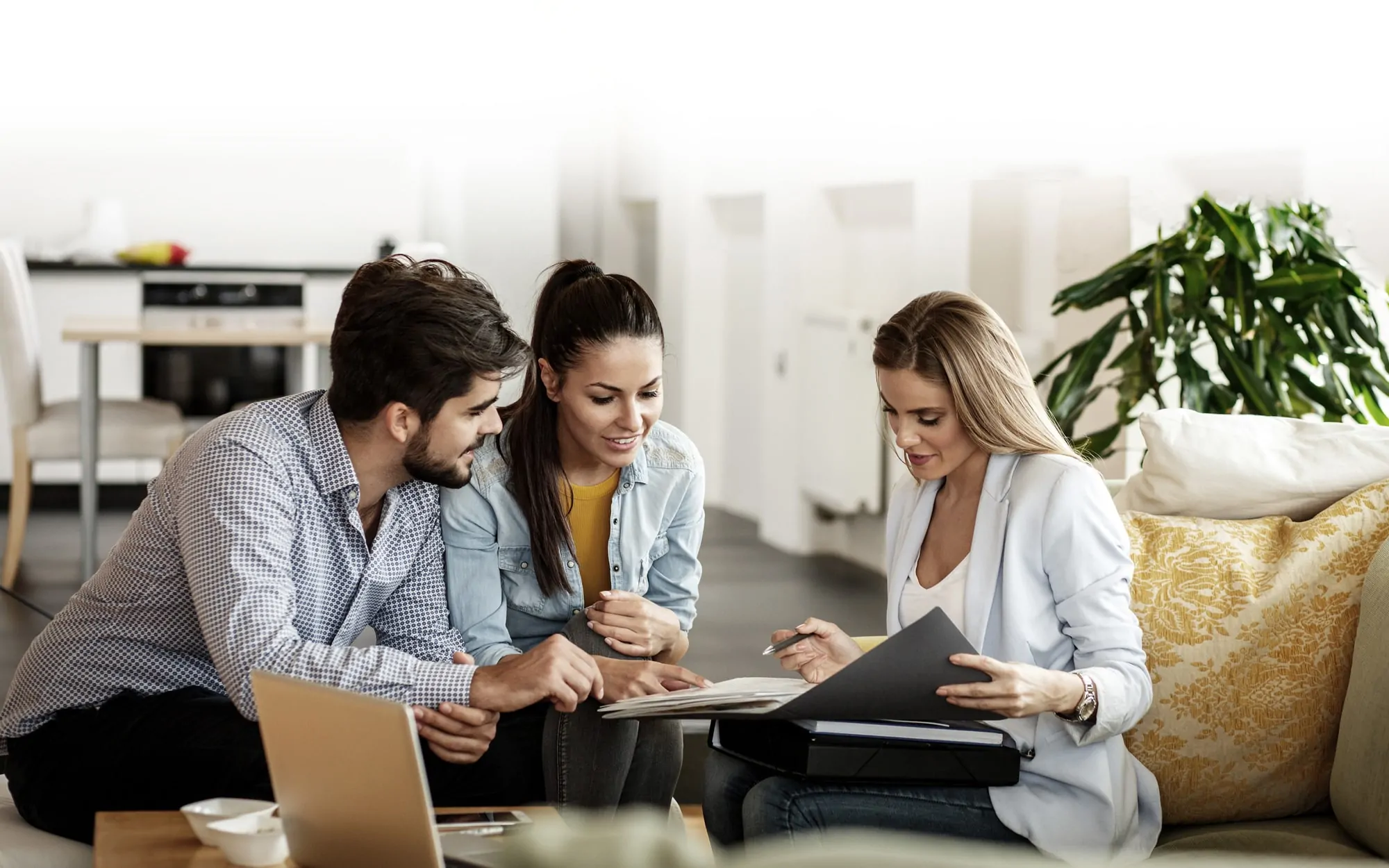 Three people sitting on a couch looking at a book.