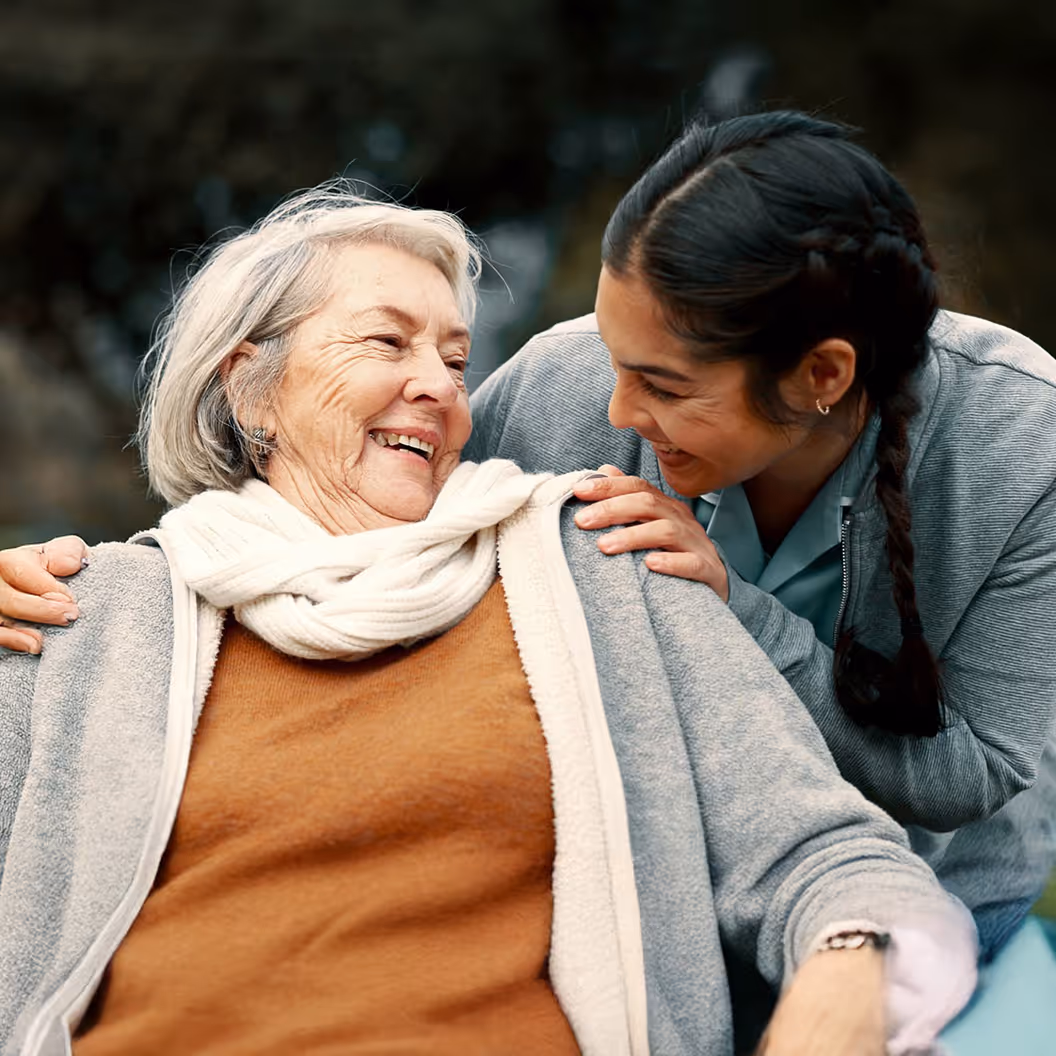 A woman hugging a woman who is sitting on a bench.