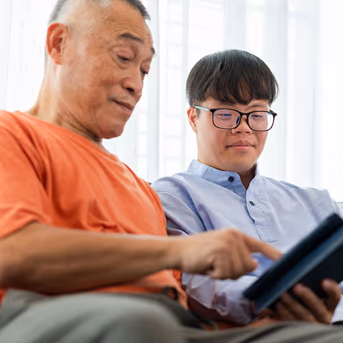 Two men sitting down whilst using an tablet device