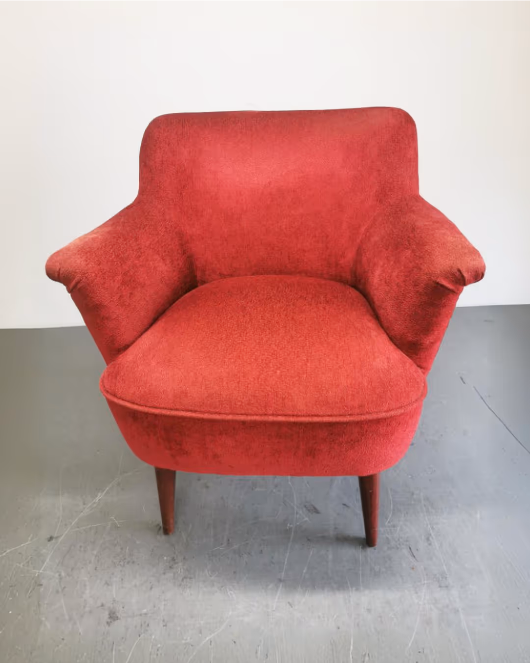 Crvena vintage fotelja s drvenim nogama na sivoj podlozi.