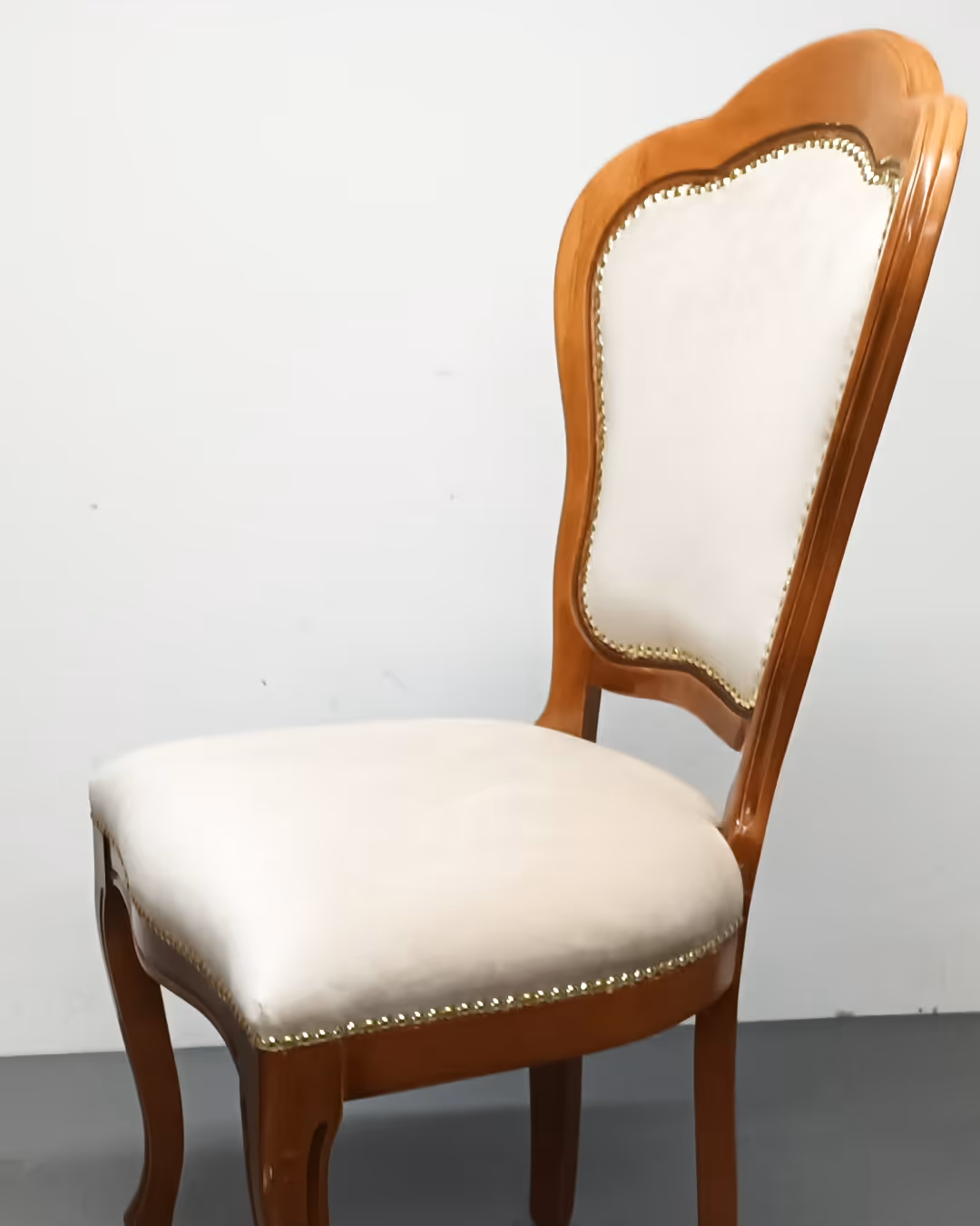 Elegantna drvena stolica s bež presvlakom i ukrasnim zakovicama.