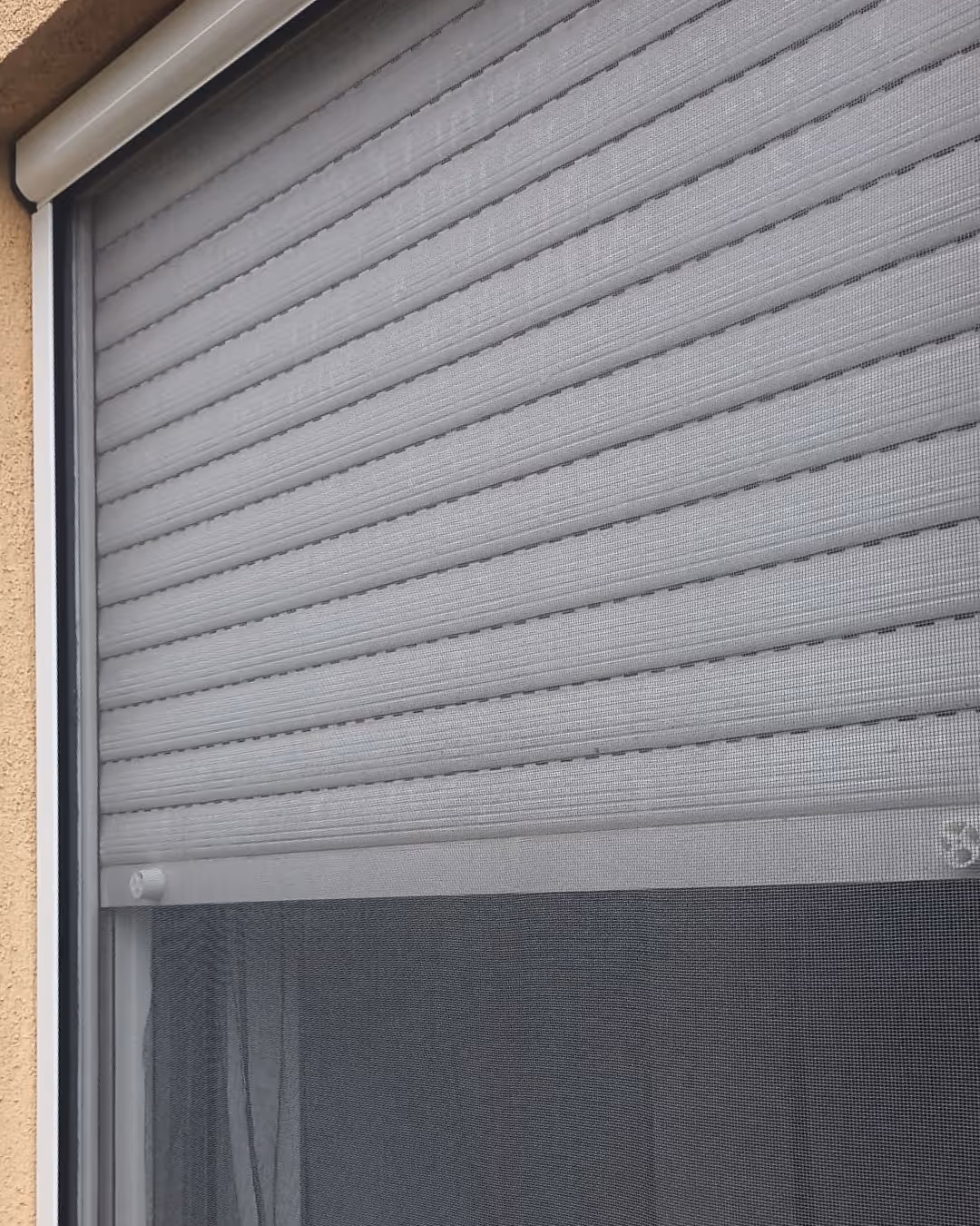 Prozor s bijelim vanjskim roletama i mrežom protiv komaraca.