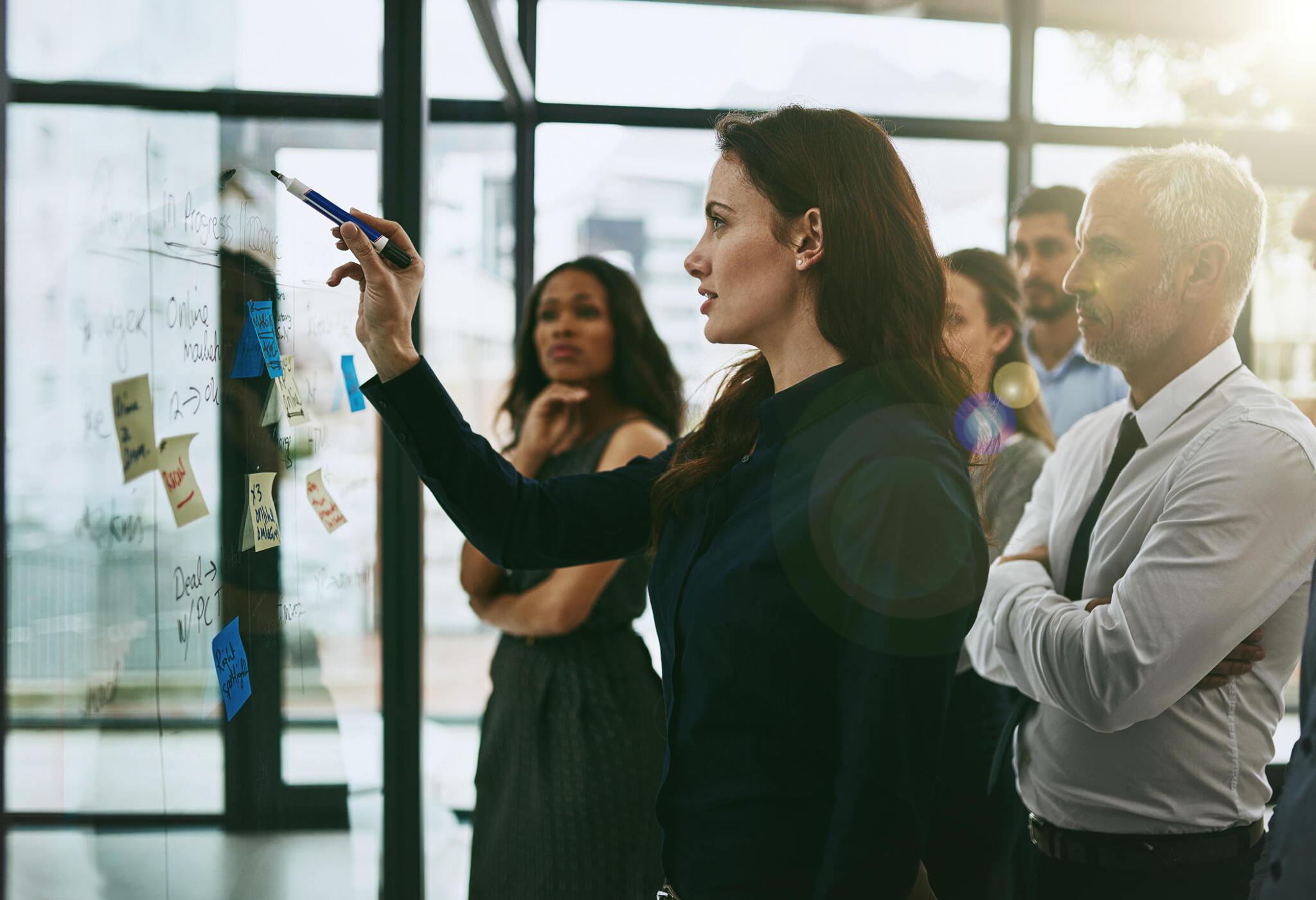 A woman leading a planning discussion at a glass board.