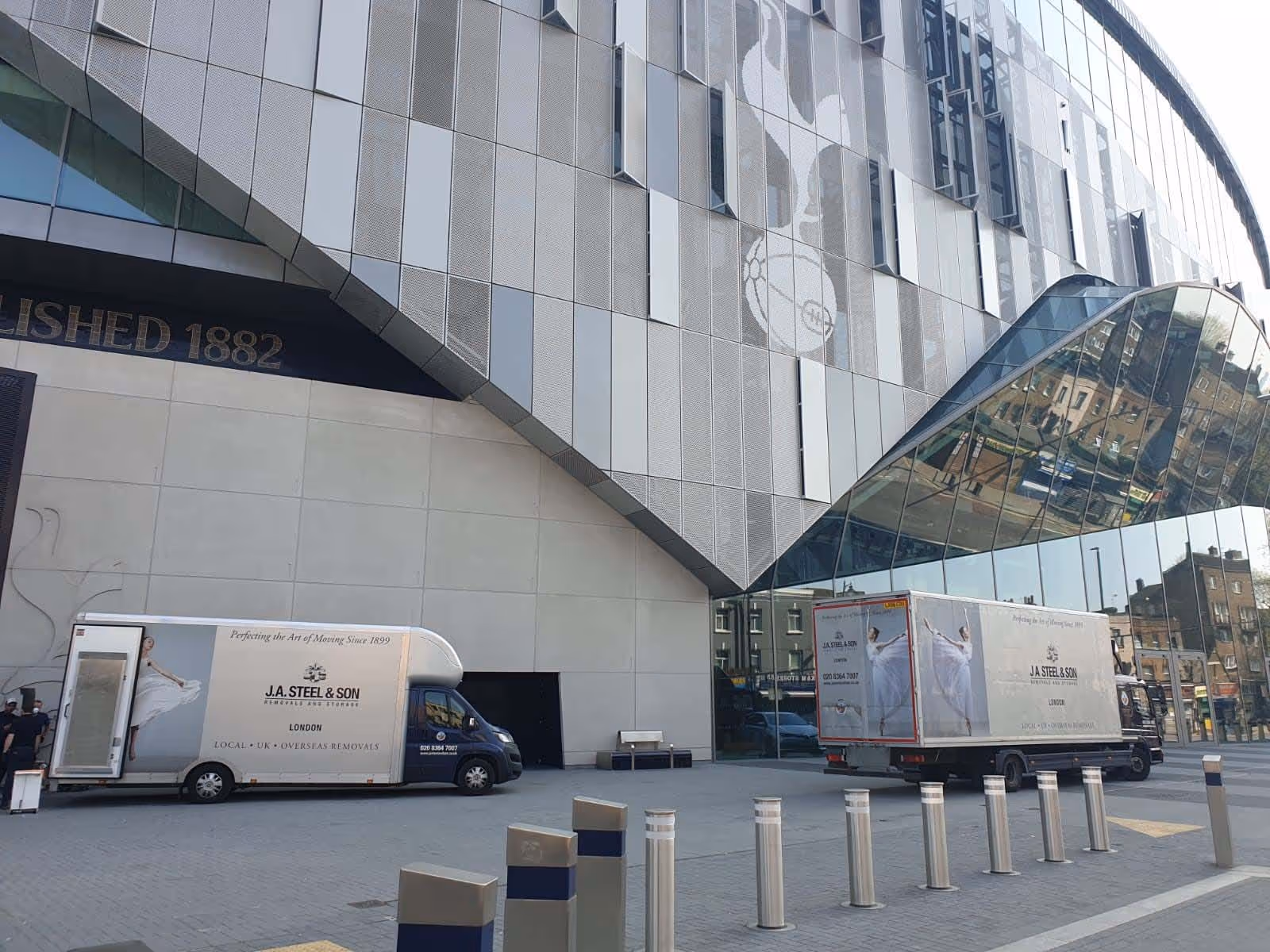 Two moving trucks parked outside a modern building with reflective glass and a white emblem.