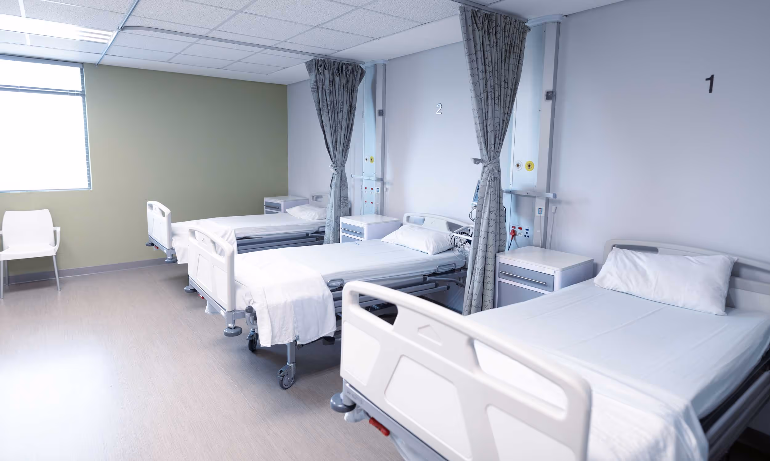 Three empty hospital beds with white sheets in a clean, well-lit room.