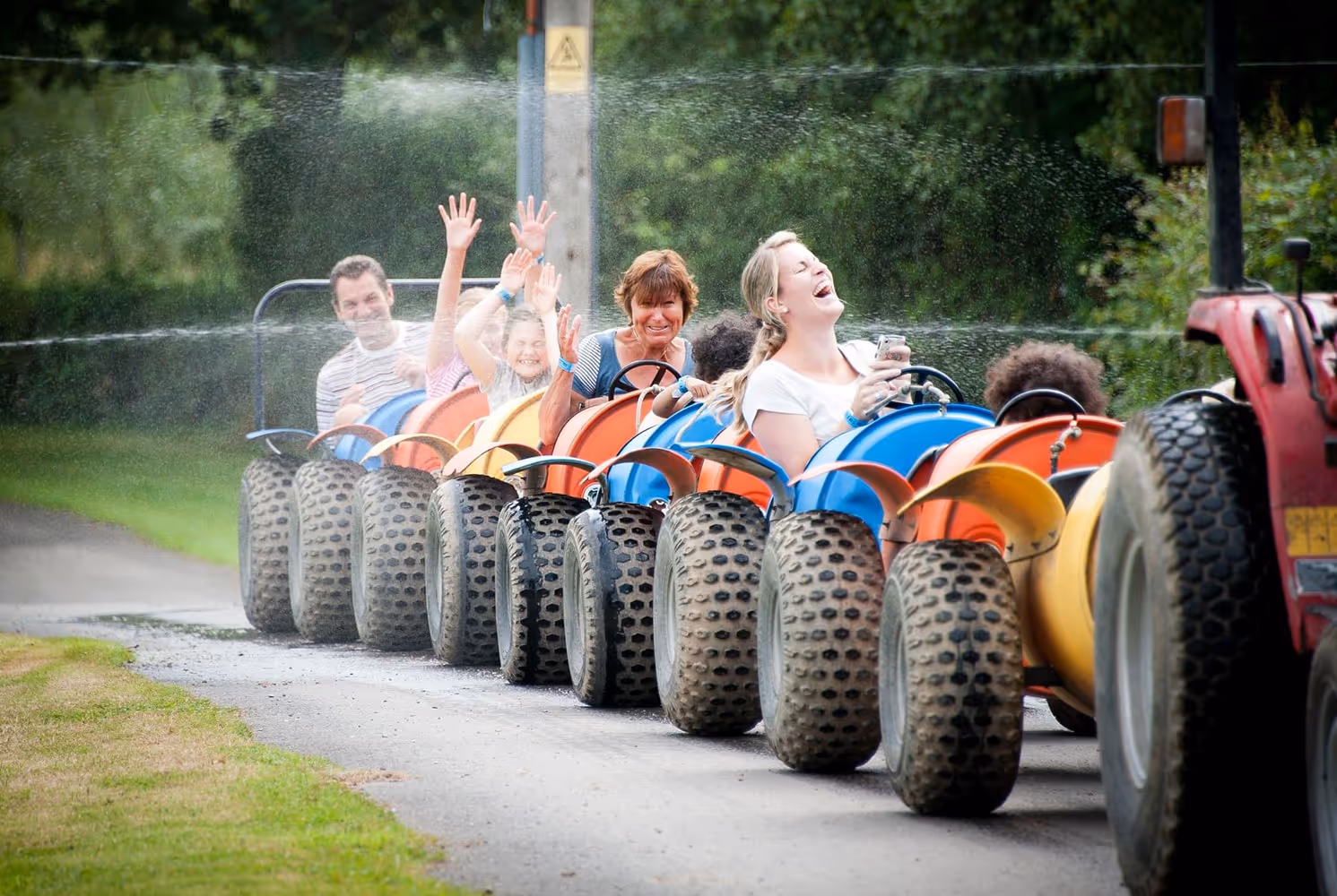 Tractor train pulling some people who are laughing and happy as they are sprinkled with water.