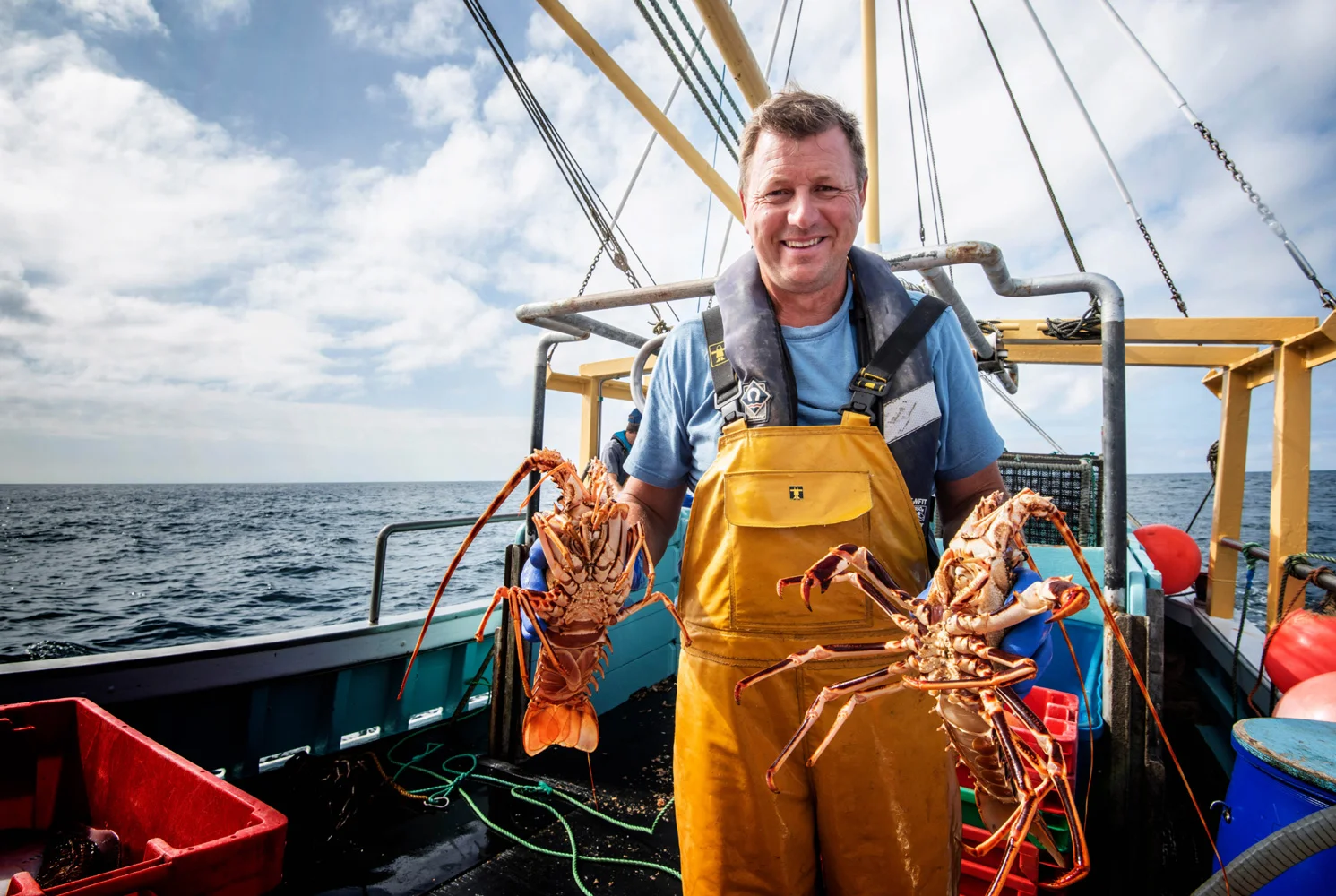 A lobster fisherman on a boat displaying his lobsters that he caught.
