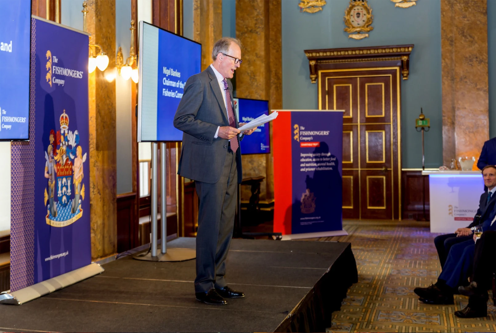 Man presenting a Fishmonger's Company presentation with branded signs in blue.