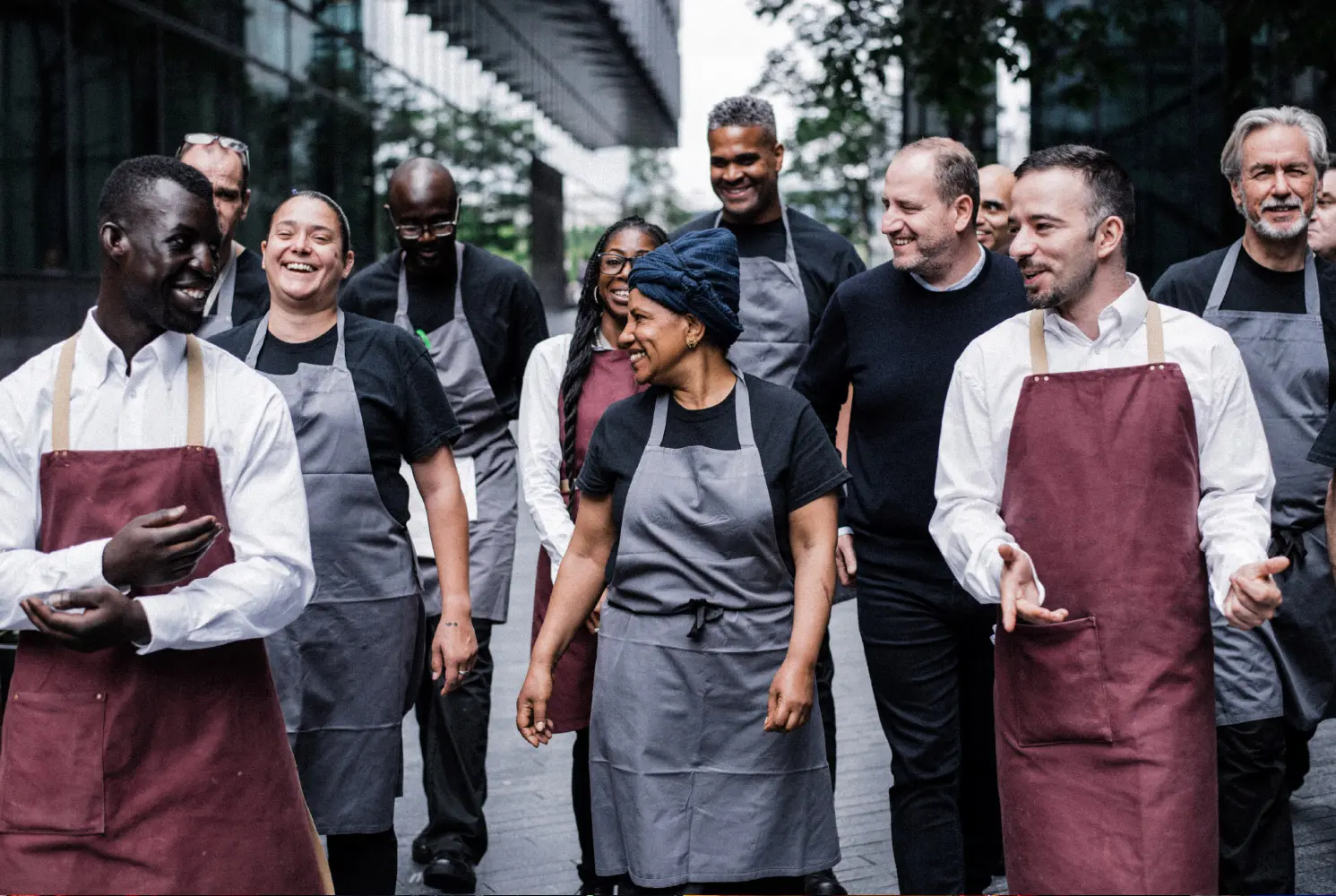 A group of Fishmongers with a mixture of red and grey aprons walking through the street, all are happy.