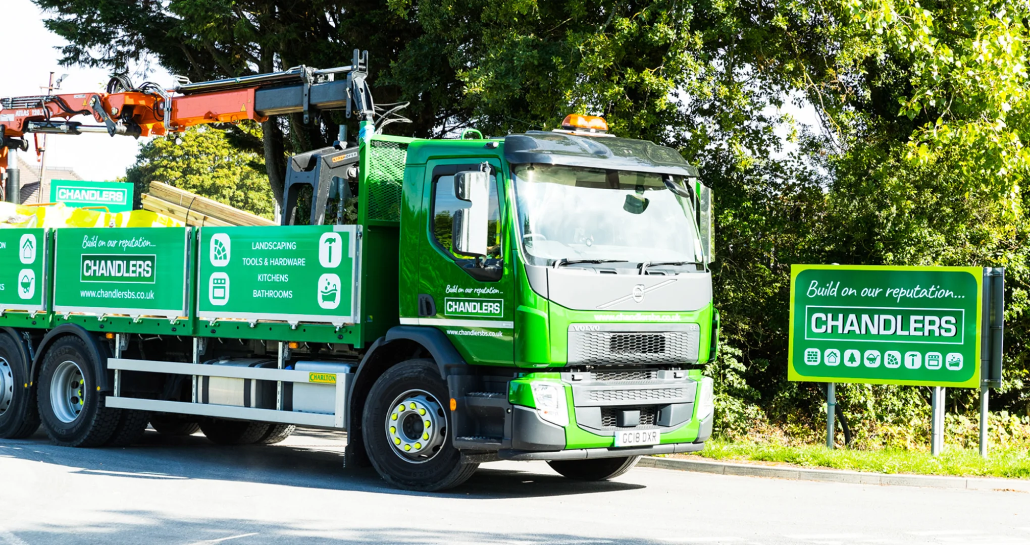 Green Chandlers Builders Merchant lorry with branded sign-writing next to a green sign. 