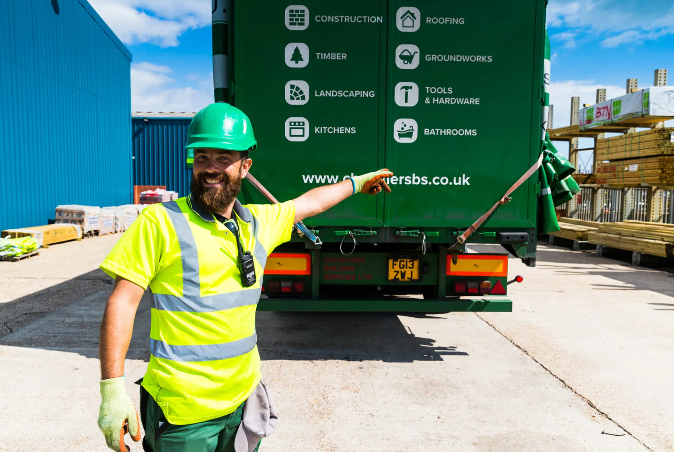 Man in a high-visibility shirt with a green hardhat pointing at a green chandlers builders merchant branded lorry.