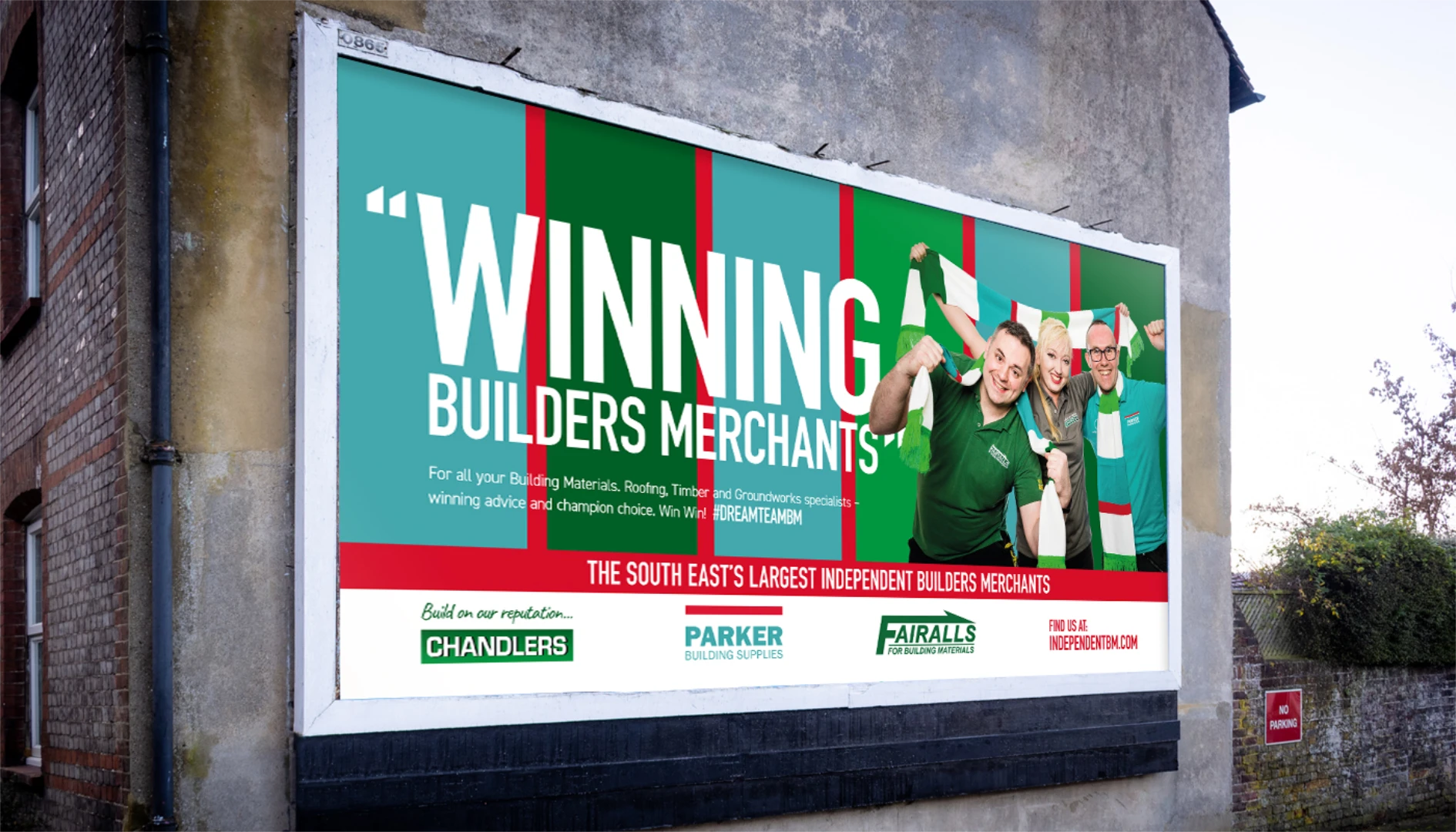 A billboard advertising "Winning Builders Merchants" with happy people in green blue and red. For Independent Builders Merchants Group.