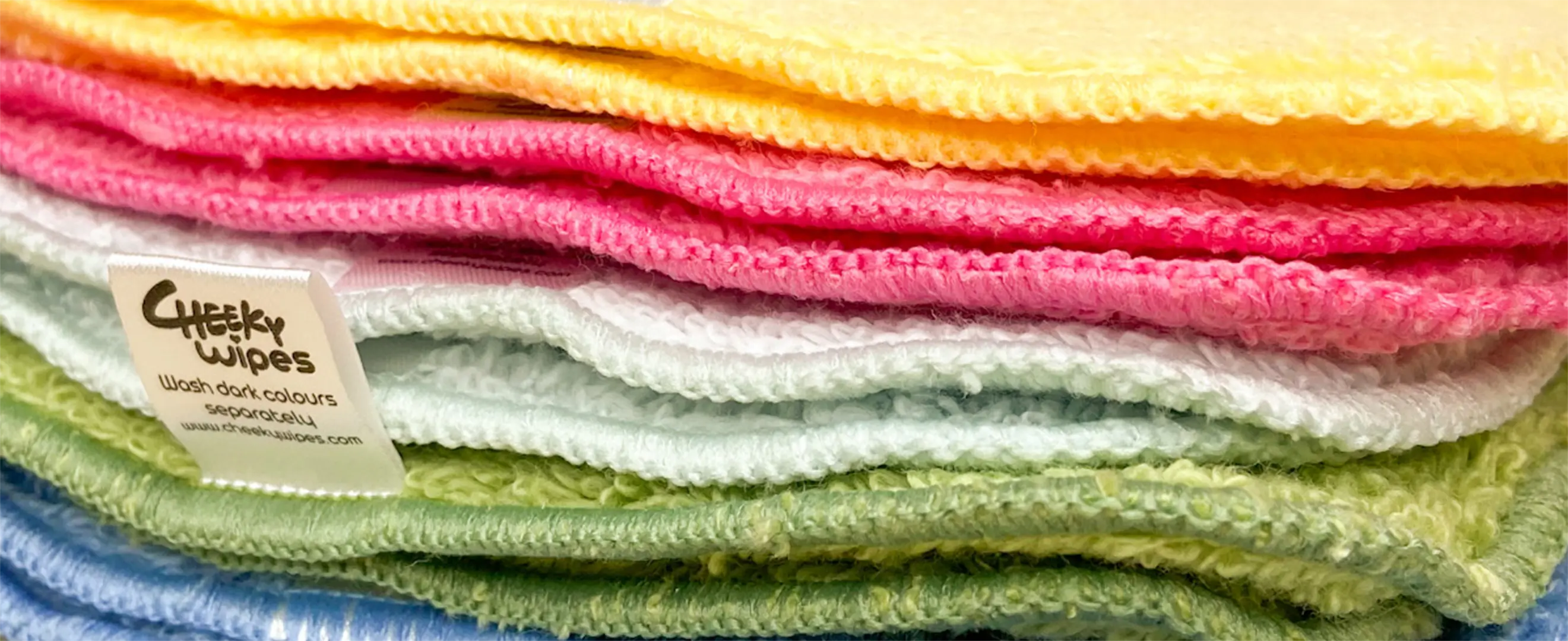 Stack of colorful microfiber cleaning cloths with a Cheeky Wipes label advising to wash dark colors separately.