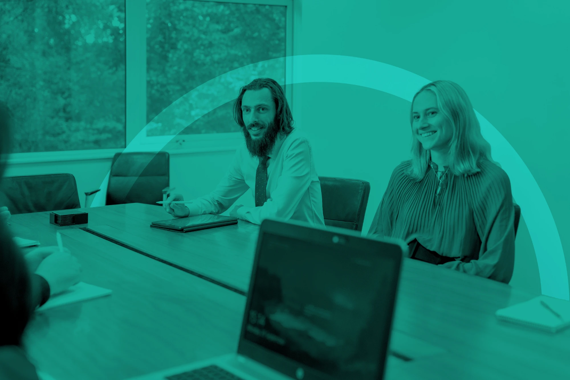 Man and woman sitting on a conference table with a circular ring shape wrapping around them with a turquoise overlay.