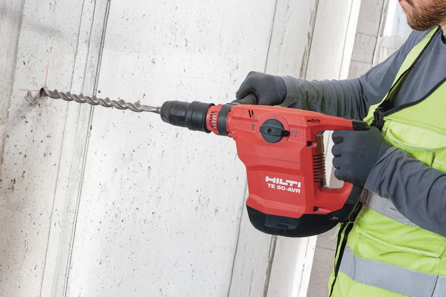 A man dressed in grey with a high visibility vest drilling into a concrete wall with a HILTI drill.