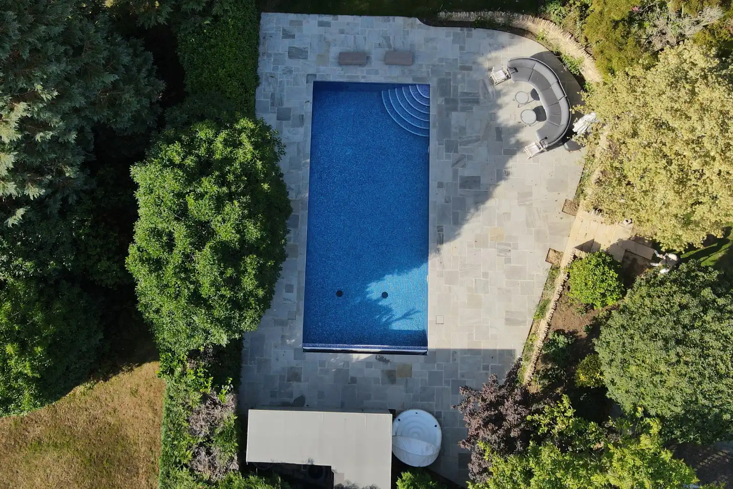 Birdseye view of a large swimming pool with sandstone paving around it.