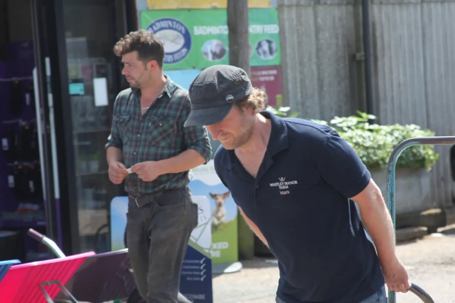Man pushing a wheelbarrow in a blue Whipley Manor Farm polo shirt.