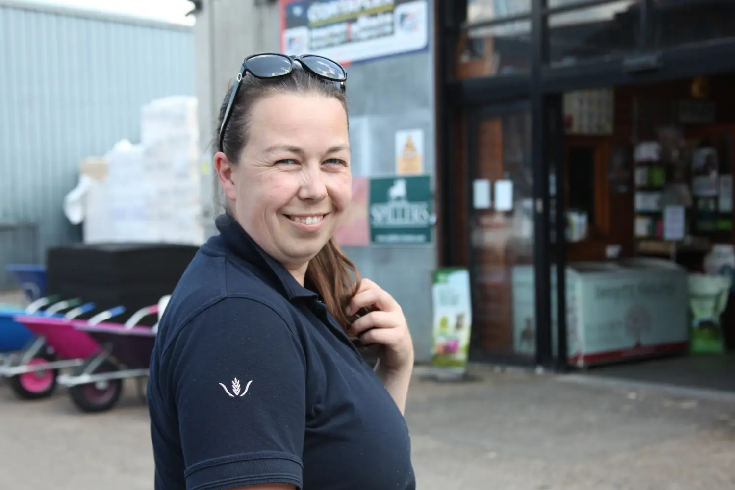 Woman outside Whipley Manor Farm Animal Feeds with a branded blue polo shirt smiling.