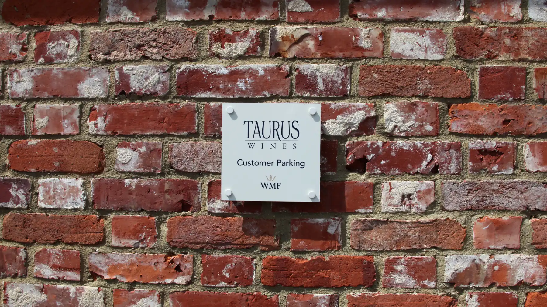Whipley Manor Farm branded building signage for Taurus Wines on a red brick wall.