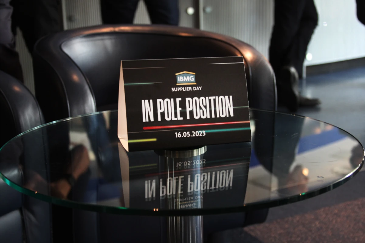 IBMG In Pole Position branded self standing sign on a small glass table.