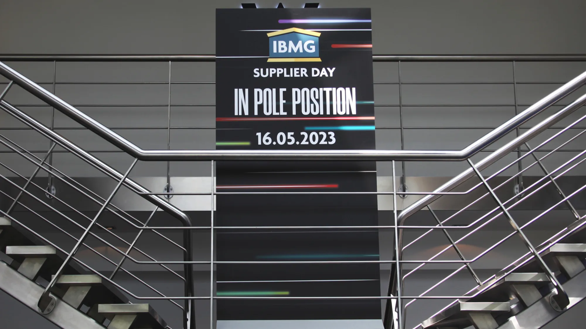 IBMG Pole Position branded banner in a stairwell with metal railings.