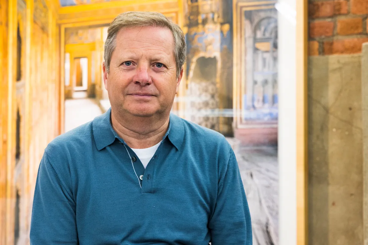 Man with short grey hair and a blue long sleeved polo shirt looking at the camera.