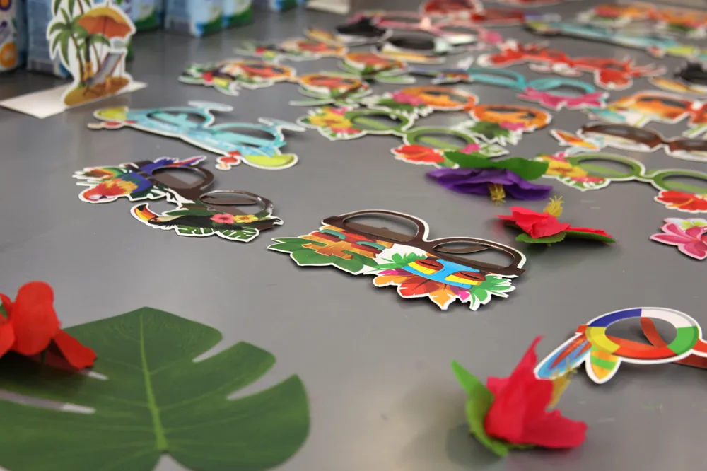 Colorful tropical-themed paper eyeglass frames and artificial flowers arranged on a table.