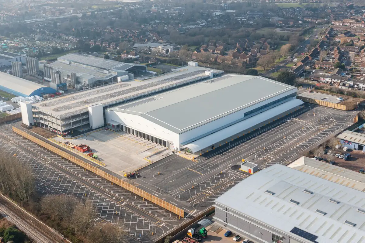 Aerial view of a large industrial warehouse with adjacent parking lots and a surrounding urban residential area.