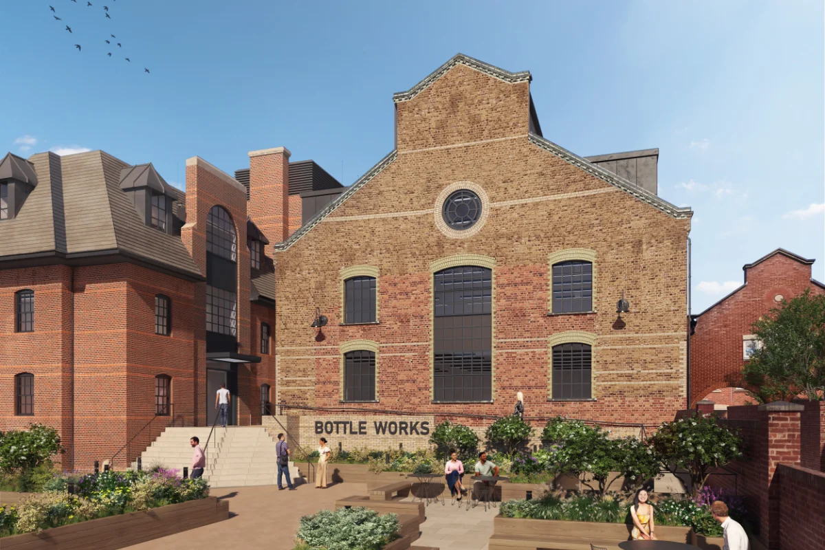 Brick building with sign 'Bottle Works' surrounded by people sitting and walking in a landscaped courtyard under a clear blue sky.