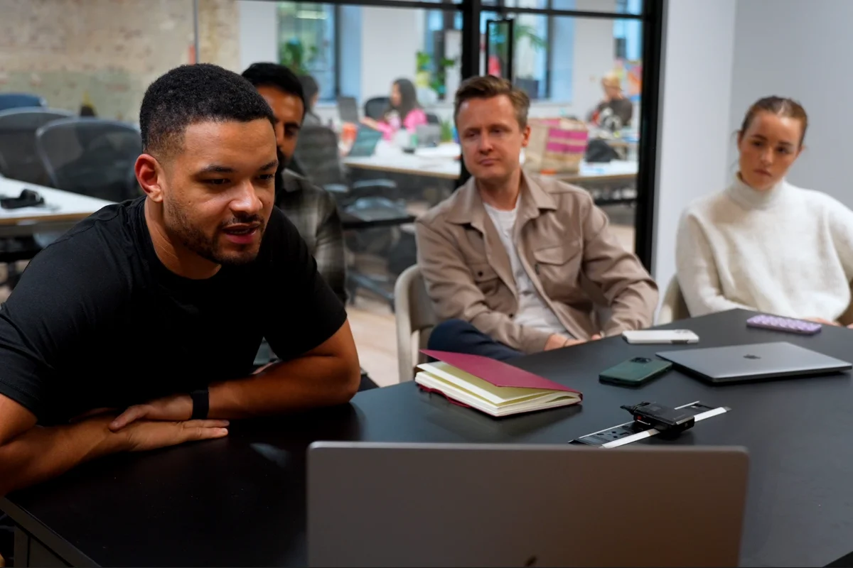 Steven Bartlett and 3 people sitting at a table watching a laptop screen in a modern office setting.