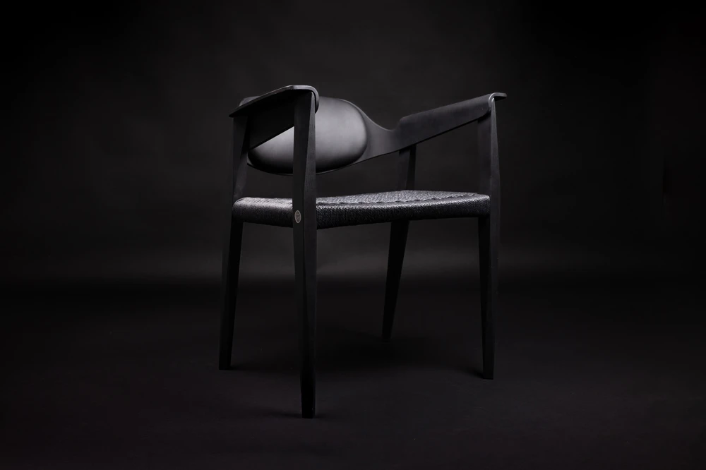 Modern black chair with woven seat and curved backrest on a black background.