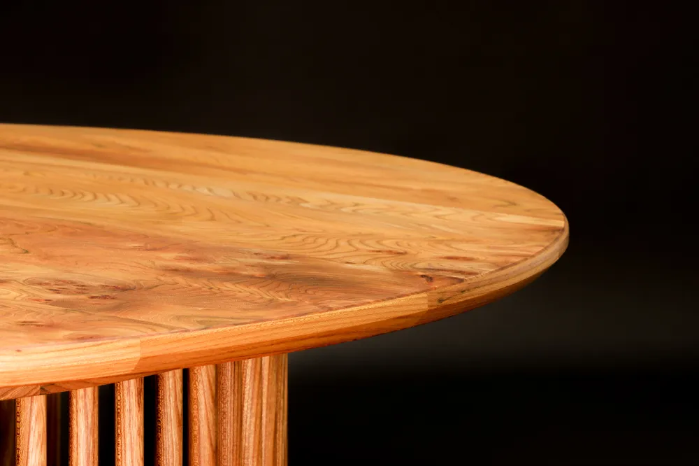 Close-up of a round wooden table with visible natural grain and a slatted wooden base against a dark background.