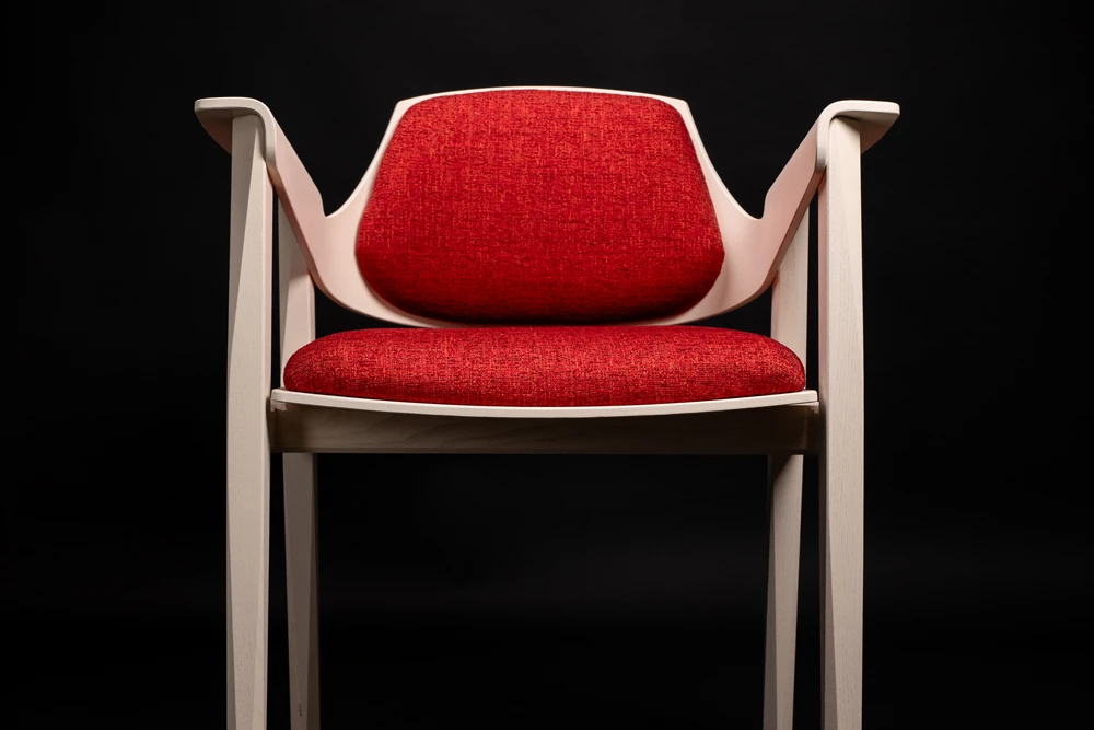 Modern chair with white wooden frame and red upholstered backrest and seat cushion against a black background.