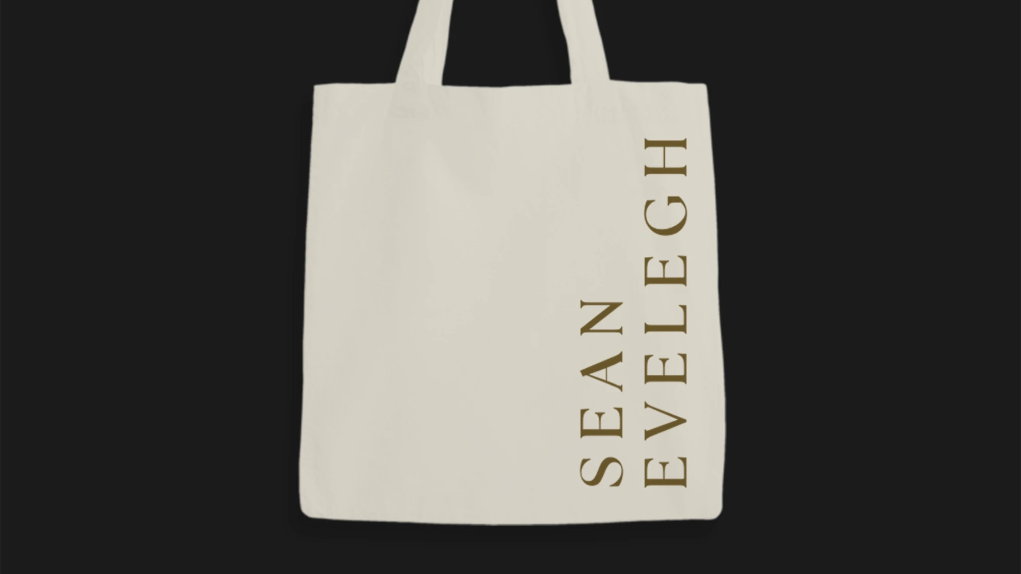 Beige tote bag with vertical text reading 'SEAN EVELEIGH' in brown letters on the right side.