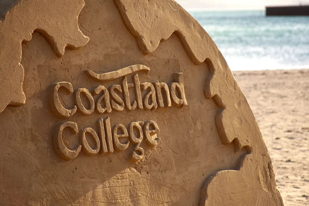 A large sand sculpture with the Coastland College logo sculpted into it.